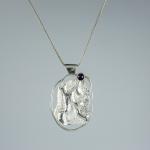 A photograph of a silver pendant with a small amethyst on a delicate silver chain.