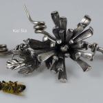 Photograph of a metallic floral brooch next to a dead bee.
