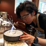 Photograph of a jeweler using a handheld torch to solder metal in a pan of small stones.
