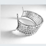 Photograph of a silver-toned, wire-mesh cuff bracelet on a white background.