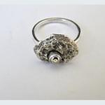 Photograph of a silver ring featuring a textured, organic-shaped setting with a small center stone.