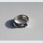 Silver ring with a small blue gemstone on a textured white surface.