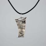 Photograph of a textured, asymmetric silver pendant on a black cord.