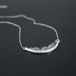 Silver crescent-shaped pendant necklace on a dark background.