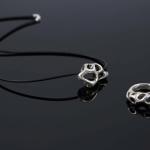 Photograph of a silver organic-patterned pendant necklace and matching ring on a dark surface.
