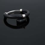 A black rubber and silver bangle bracelet reflected on a dark, glossy surface.