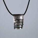 Photograph of a layered, textured silver pendant on a black cord.