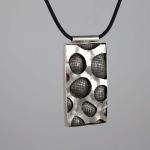 Rectangular silver pendant with a textured, porous pattern on a black cord necklace.