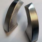 Photograph of two curved, brushed metal components against a plain white background.