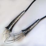 A statement necklace with textured silver metal cones and a wire cage pendant on a black cord.