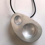 Photograph of a silver-toned, abstract pendant with two circular cutouts on a black cord.
