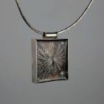 Photograph of a rectangular silver pendant containing a textured gray element and a small dark bead.
