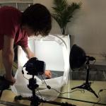 Photographer arranging a small object inside a lit tabletop photography studio.