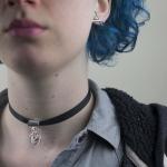 A person with blue hair wears a black ribbon choker with a silver charm and a small earring.