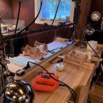 Photograph of a workshop bench with tools, wooden crafts, and hanging lights.