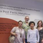 Photograph of four smiling artists in front of exhibition wall text.