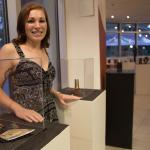 Photograph of a woman smiling beside glass display pedestals in an art gallery.