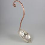 Photograph of a silver ladle with a copper handle, on a neutral gray background.