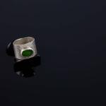 Photograph of a silver ring with a green stone on a black surface.