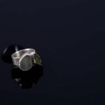 A silver ring with two sea glass stones on a dark reflective surface.