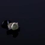 Photograph of a silver ring with a pale green stone on a black surface.