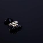 A silver ring with cluster beads sits on a black reflective surface against a dark background.