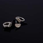 A photograph of two silver rings with citrus-slice motifs resting on a black surface.
