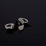 Photograph of three silver rings with half-circle designs on a dark, reflective surface.