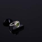 Photograph of a silver ring with a green stone on a black surface.
