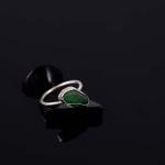 Photograph of a silver ring with a green sea glass stone on a black surface.