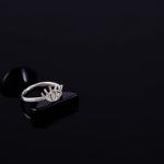 A silver ring with an eye design rests on a black stand.