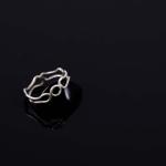 Photograph of a silver ring with interconnected loops on a black reflective surface.