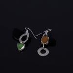A photograph of two asymmetrical earrings with sea glass and silver on a dark background.