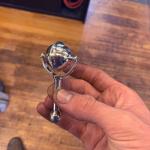 Photograph of a hand holding a small, shiny metal baby rattle.