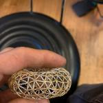 Close-up photograph of a hand holding a small, intricate, silver geometric donut..