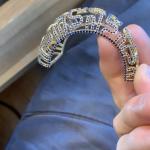 A hand holding an ornate gold bracelet encrusted with blue stones.