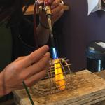 A close-up photograph of a person using a blowtorch to solder a metal cage.