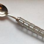 A silver spoon with an ornate, caged handle on a white surface.