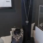 Photograph of silver jewelry displayed on black stands in a gallery.
