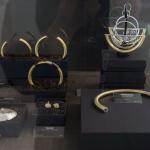 Gold and silver jewelry displayed in black boxes in a glass case.
