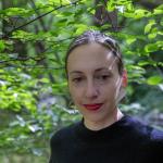 A photograph of a woman wearing a black sweater in a lush green forest.