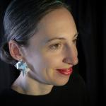 Photograph of a woman with red lipstick and silver origami earrings against a black background.