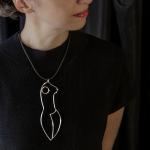 A woman wearing a large, abstract female-form pendant necklace.