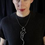A woman in a black shirt wears a silver pendant resembling a human figure.