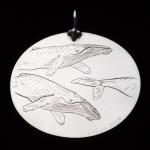 Circular silver pendant with etched illustration of three swimming whales.