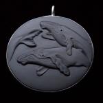 A round dark gray pendant featuring a relief carving of three whales.