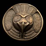 Photograph of a round bronze medallion featuring an owl face and feathers.