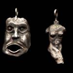 Photograph of two silver pendants: one shaped like a screaming face, the other like a torso.