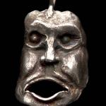Photograph of a silver pendant shaped like an expressive, grotesque human face.