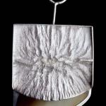 Photograph of a silver pendant with a textured rectangular top and a curved base made of moose hoof.